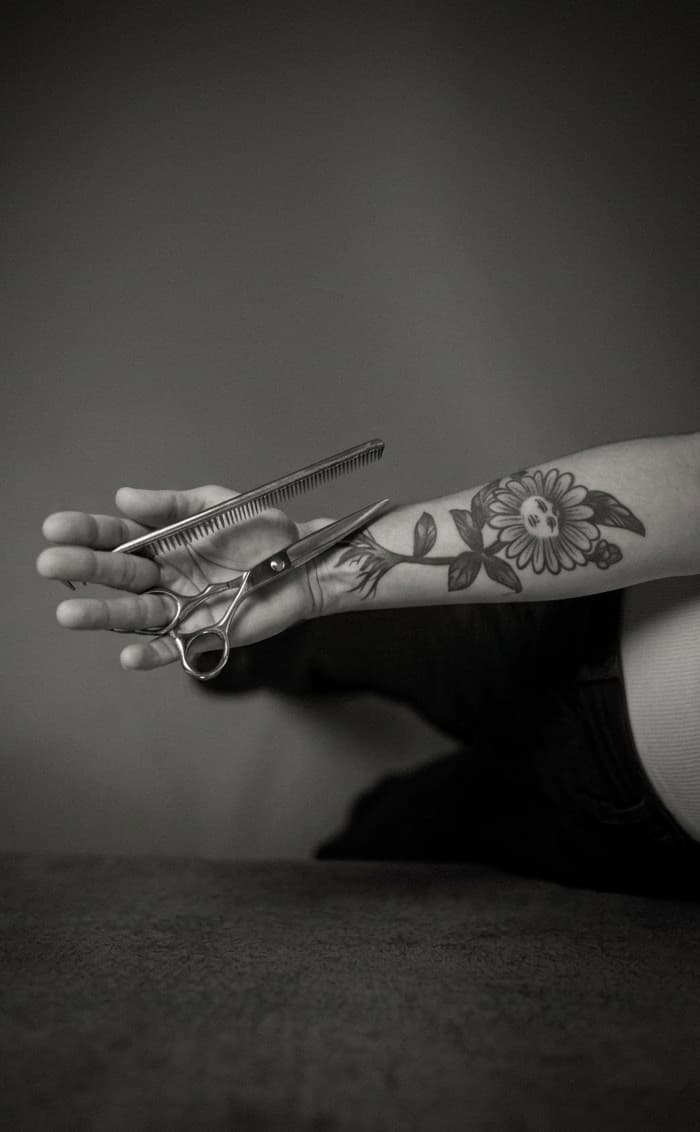 Mano tatuada sosteniendo tijeras y peine