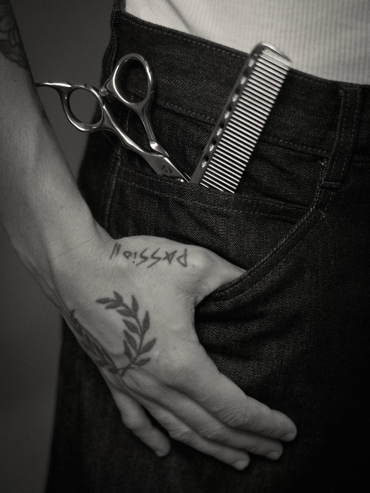 Tijeras y peine en el bolsillo del vaquero, mano tatuada con «passion»
